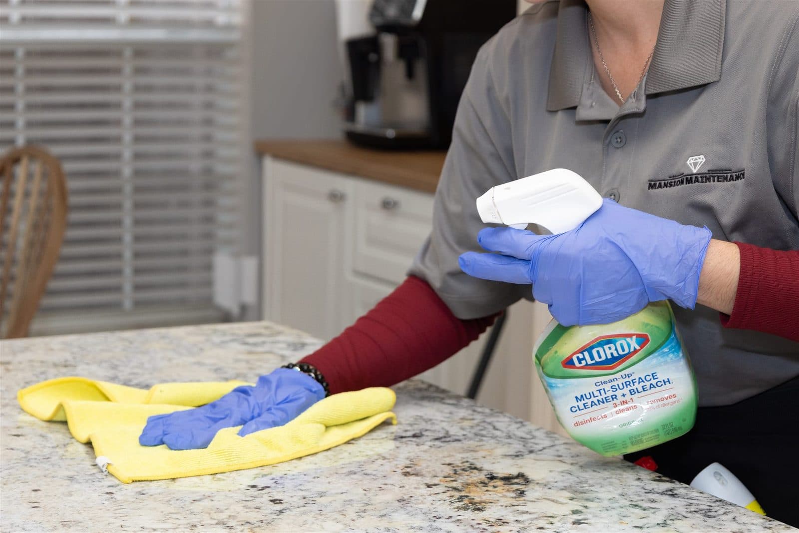 Mansion cleaner spraying and wiping a countertop in a branded polo